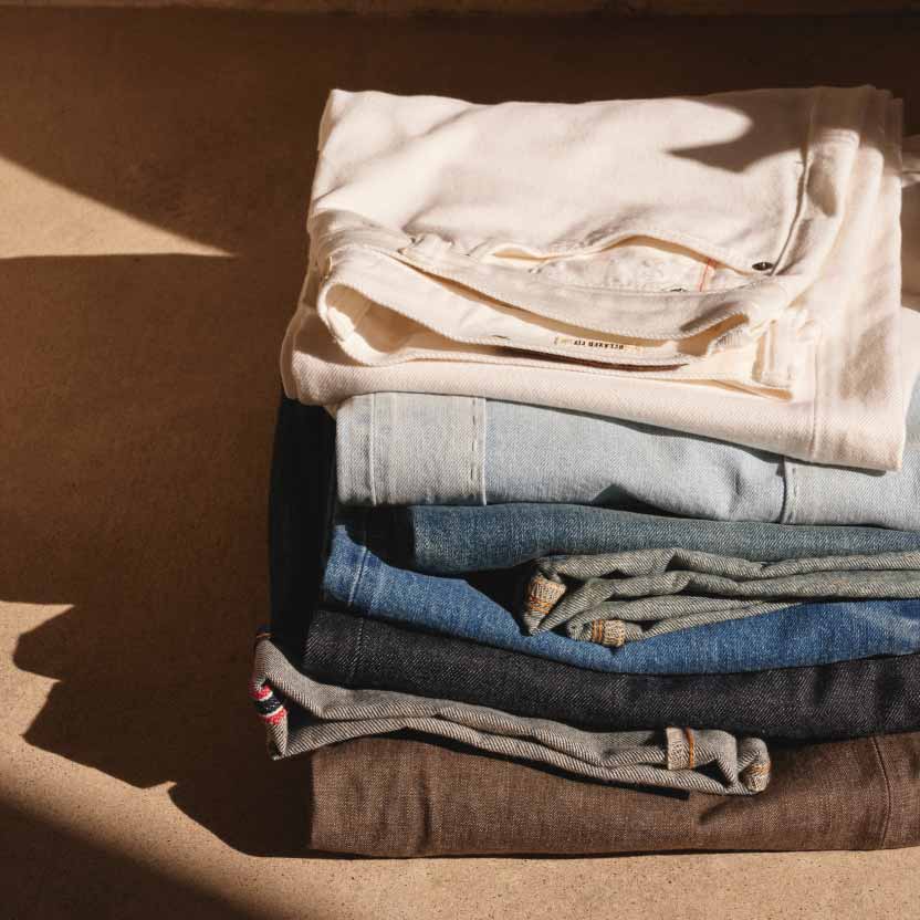 A photograph of a stack of folded denim jeans and pants in different colors and washes.