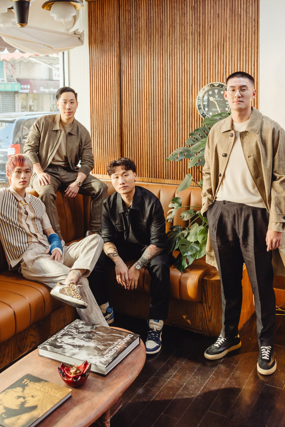 A photograph of four young Asian American men sitting and standing together in the corner of a barbershop, wearing chore coats, trousers, cashmere shirts and sweater polos.