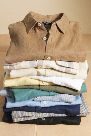 A photograph of a stack of linen button-up shirts in different colors and patterns.