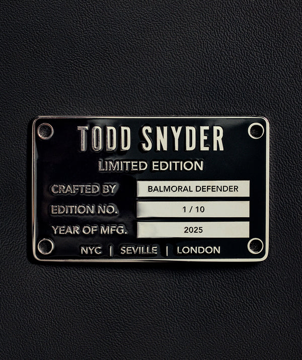 Close up of a black metal nameplate secured to leather with four rivets. The plate reads: Todd Snyder Limited Edition, Crafted by Balmoral Defender, Edition No. 1/10, Year of MFG. 2025, NYC, Seville, London.