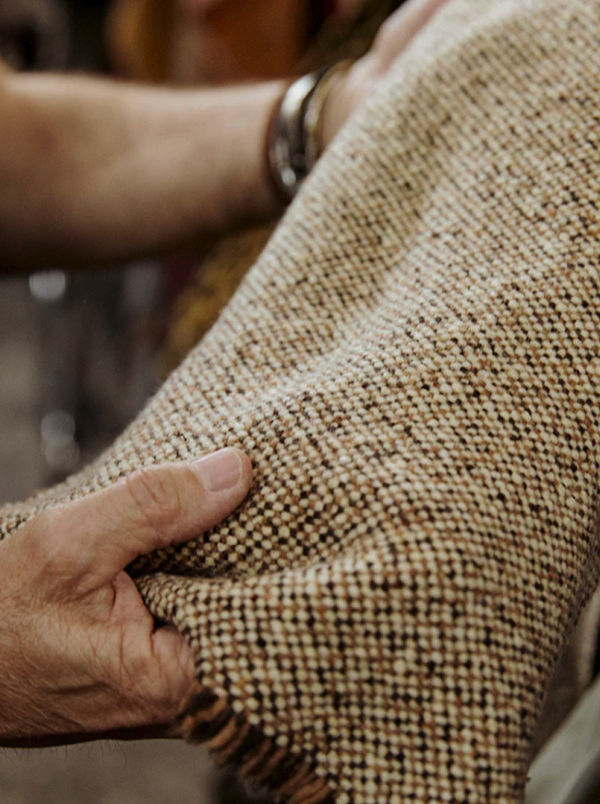 Hands closely examining a piece of textured, woven tweed fabric, with a watch visible on one wrist.
