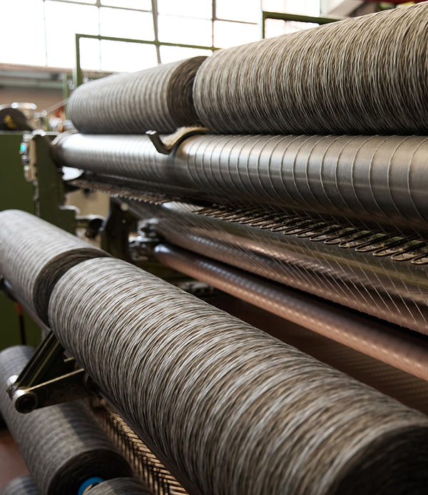 Industrial textile machinery with large cylindrical spools of dark thread wound in tight rows, photographed inside a mill.