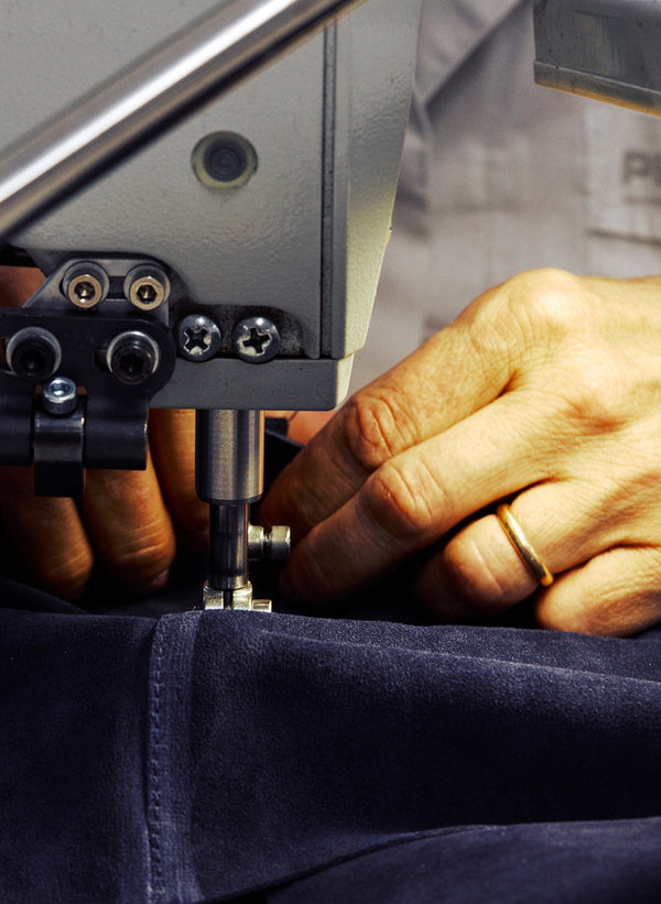 Extreme close-up of a sewing machine needle stitching into dark navy fabric, with fingers guiding the material beneath the presser foot.